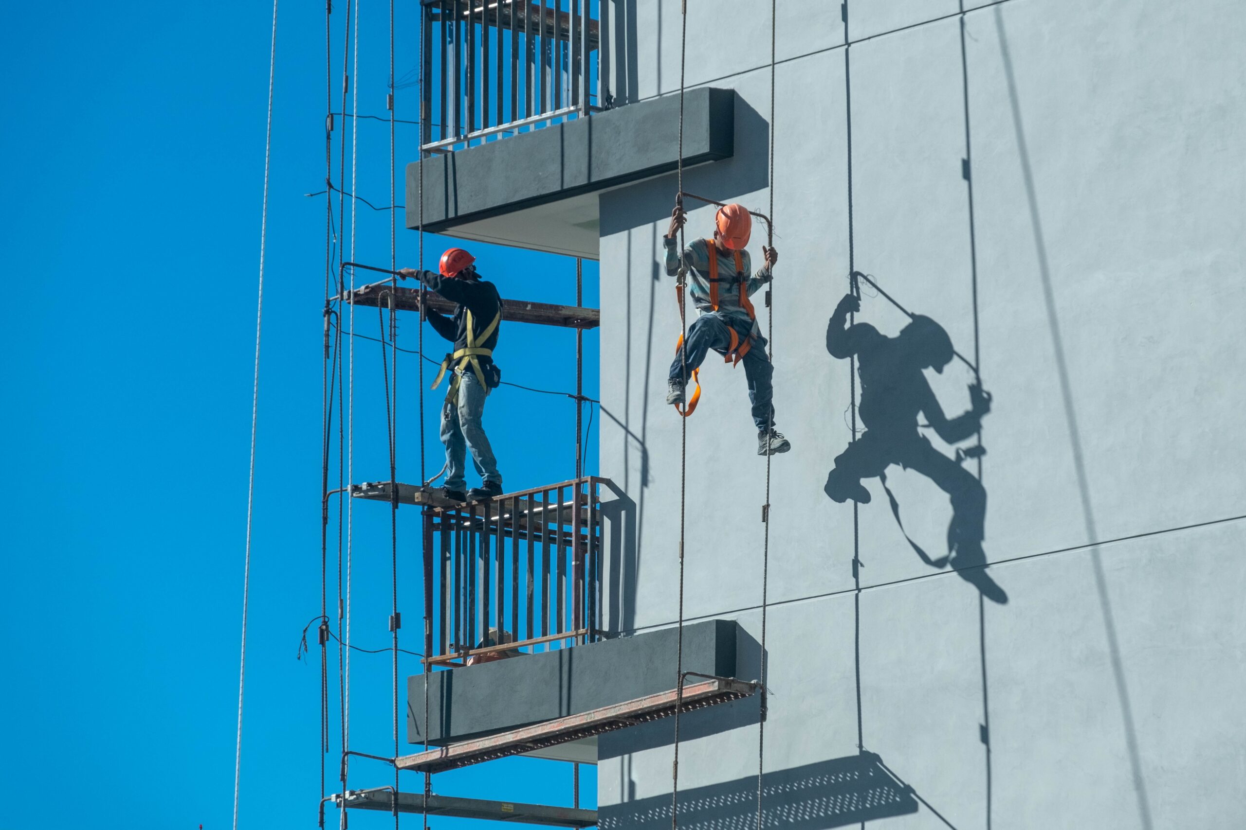 A couple of workers fixing and climbing a scaffolding while following all the safety measures